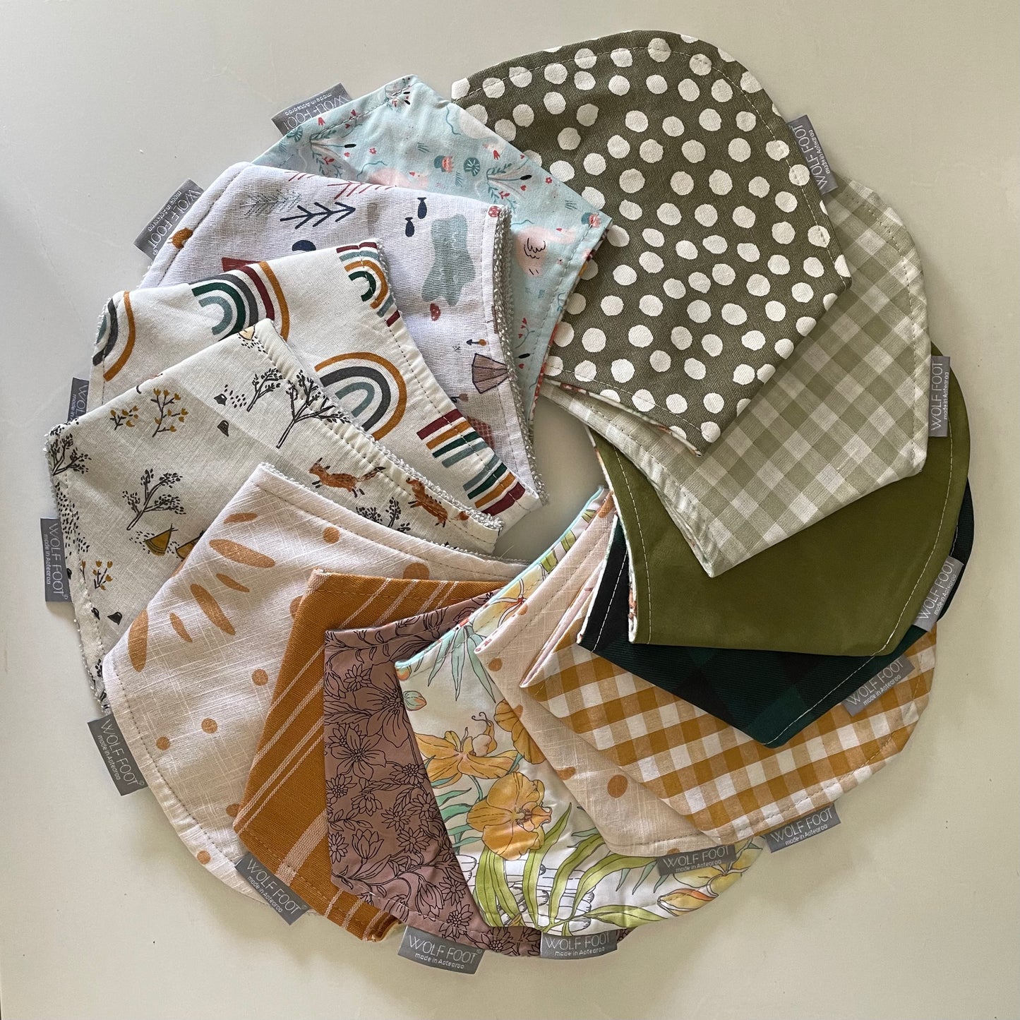 A collection of folded bandana bibs in various colors and patterns, laid out on a white surface.